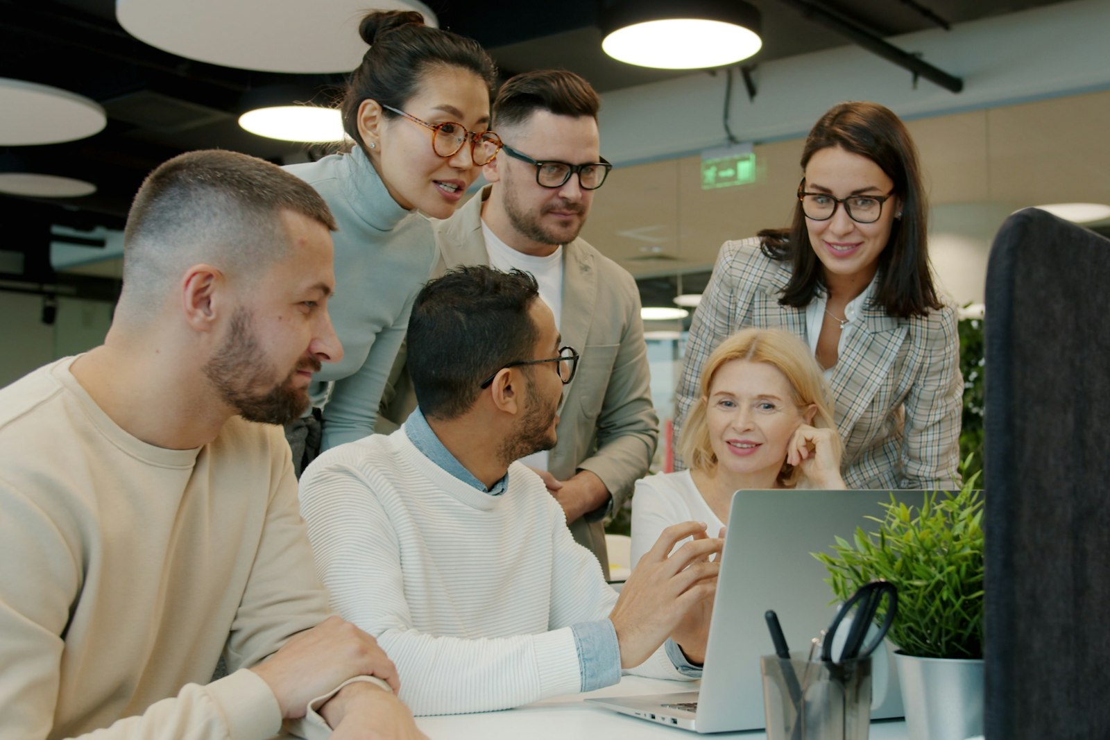 A diverse team of colleagues collaborating around a laptop in a modern office